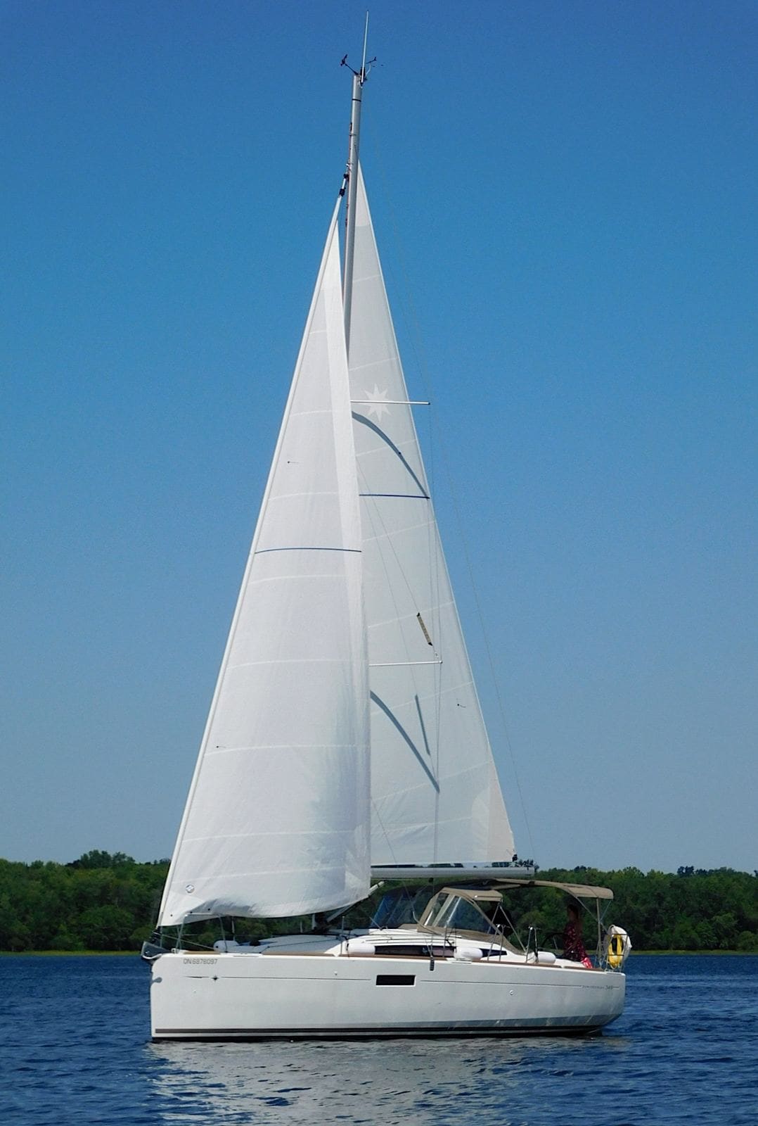 A sloop under full sail on a calm, sunny lake